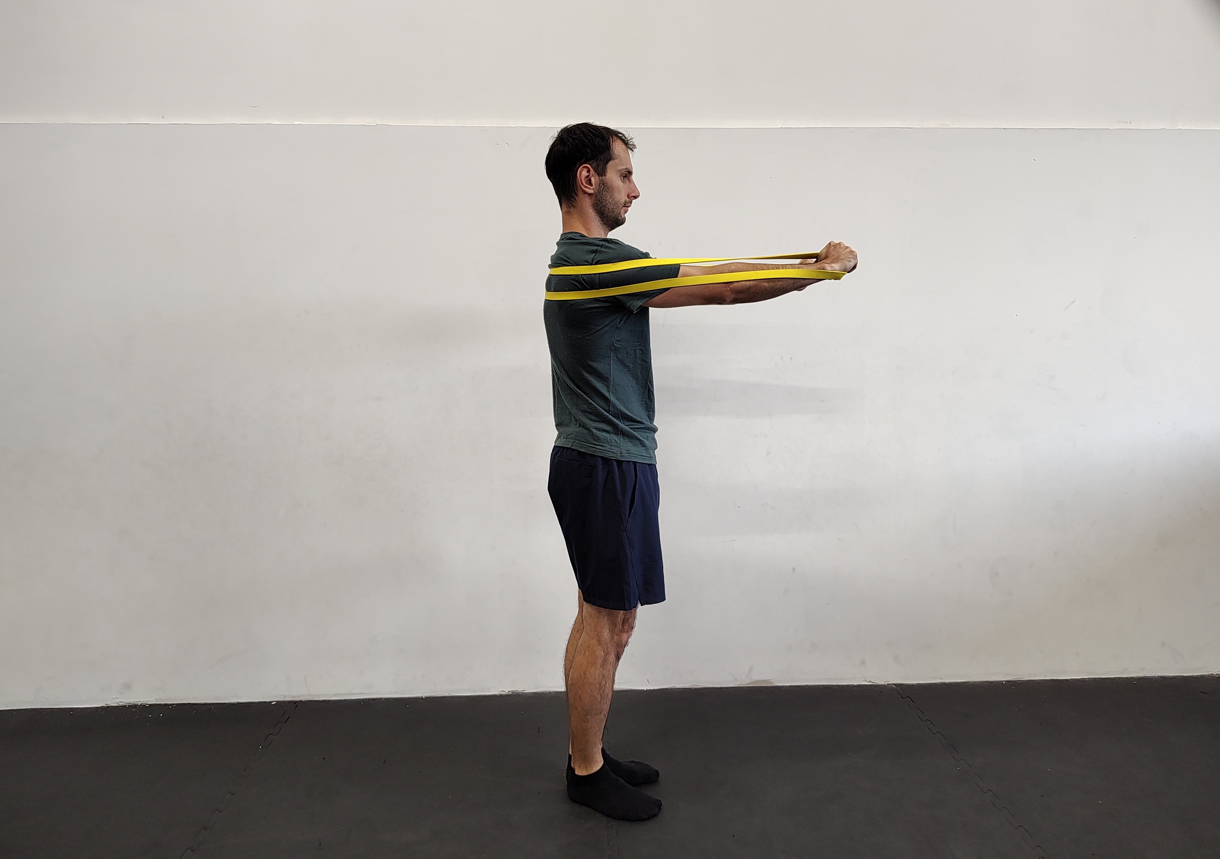 Muž v tělocvičně cvičí tlaky ve stoje s expandérem.